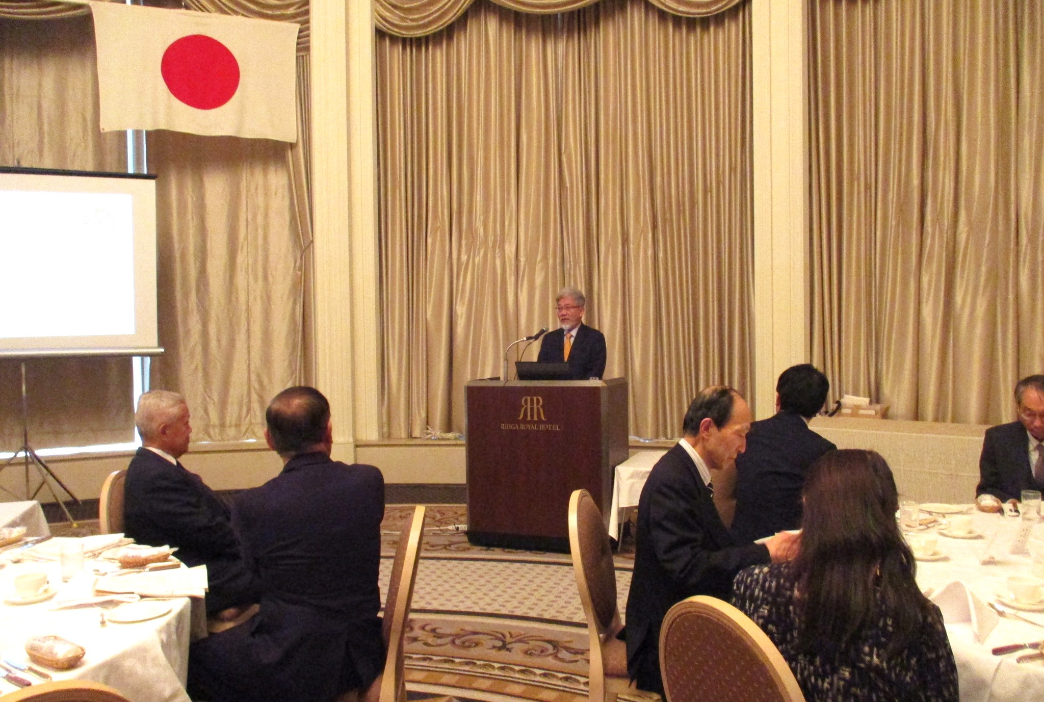 第532回国連午餐会で主催者挨拶を行う三宅善信師と講演する正木一博日銀大阪支店長